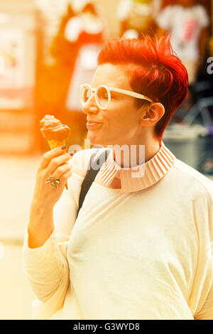 red-haried woman standing in the streets and eating chocolate icecream Stock Photo