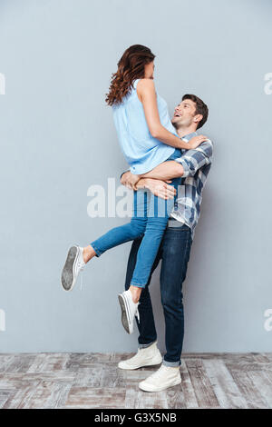 Man lifting up his girlfriend isolated on gray background Stock Photo