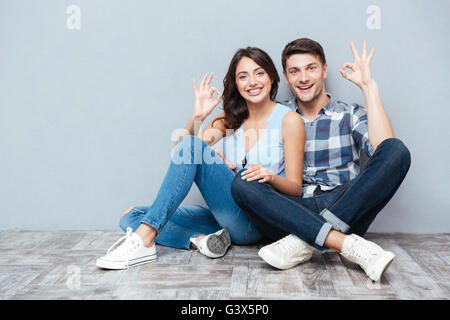 Close up of young happy couple giving thumbs up isolated on gray background Stock Photo