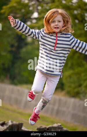 Jumping High. A  young girl attempts to spring off an old fallen tree trunk, to jump high in the air. Stock Photo