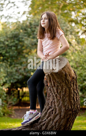Deep in Thought. A young girl has climbed a tree and is sitting comfortably thinking about something. Stock Photo