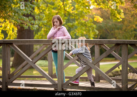 Watch that One. Two sister are duck watching from a bridge over the pond in a local park. The younger is too short to see over. Stock Photo