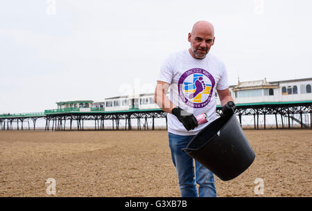 Man helping to clear litter and other rubbish from a sandy beach in Lytham St Anne's, Lancashire, UK Stock Photo