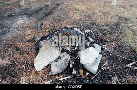 Used fire pit and cinders and ash with surrounding stones and old metal grill at camp site. Stock Photo