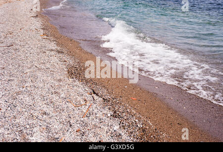 Beach of coarse sand and stones with small incoming waves breaking. Stock Photo