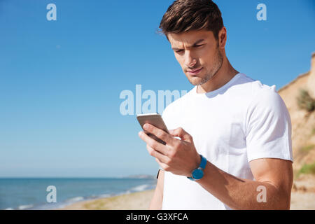 Serious atractive young sportsman using fitness tracker and smartphone outdoors Stock Photo