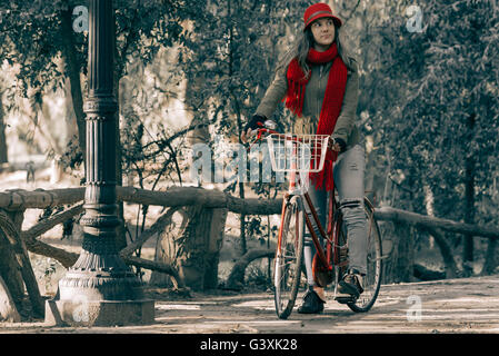 Girl riding bike at park wearing red urban fashion on beautiful autumn day, vintage contrast effect.