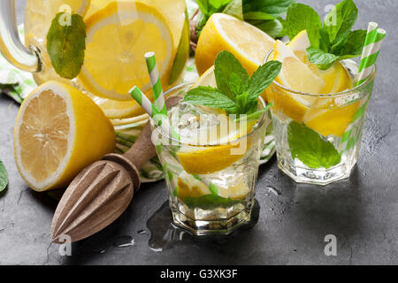 Lemonade pitcher and glasses with lemon, mint and ice on stone table Stock Photo