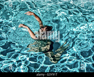 Woman in outdoor swimming pool with head submerged and arms above head Stock Photo