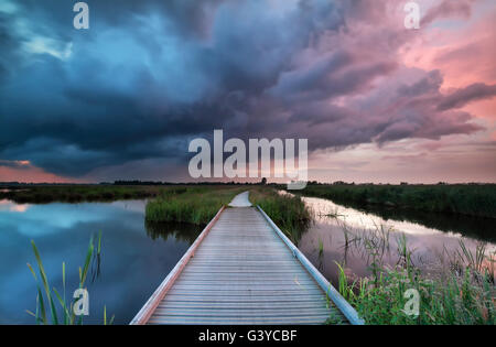 wooden path bridge over river at stormy sunset, Netherlands Stock Photo