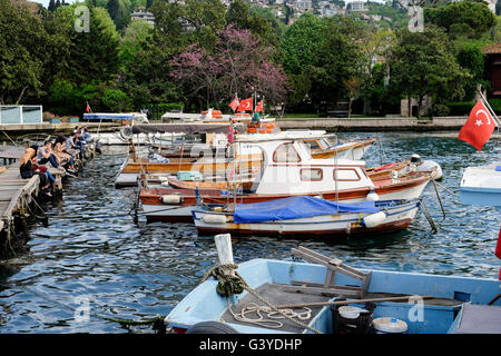 moored fishing boats on the  Bosphorus on a sunny day in Istanbul with people resting by the water Stock Photo