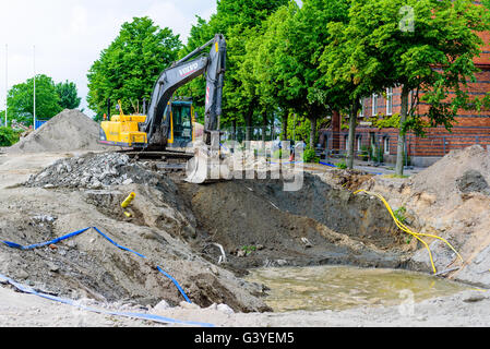 Karlskrona, Sweden - June 16, 2016: Yellow Volvo EC210 excavator digging a large hole in the ground. Water is filling up in the Stock Photo