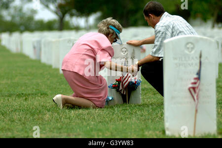 A mother and her son hold hands and pray at a grave site. Stock Photo