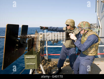 Gunner's Mate's fire a .50-caliber machine gun aboard an aircraft carrier. Stock Photo