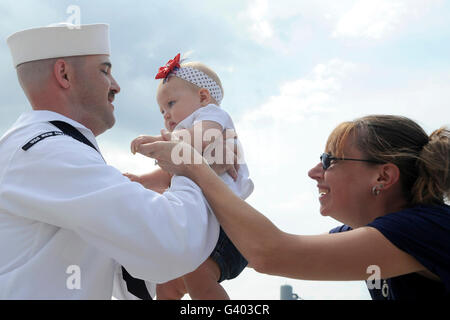 U.S. Navy sailor is handed his eight-month old daughter by his wife at homecoming. Stock Photo