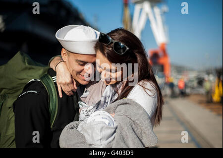 U.S. Navy sailor hugs his wife and newborn child. Stock Photo