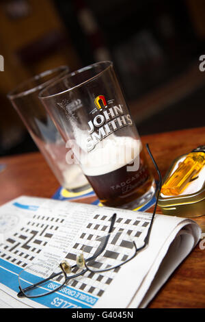 A lunch break view of the days local crossword puzzle with the remains of a pint of beer/ale in an English pub/bar. Stock Photo