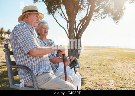 Side view shot of senior man and woman sitting on a park bench outdoors. Retired couple sitting on a park bench and looking at a Stock Photo