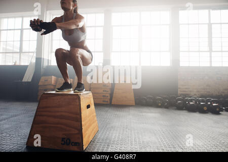 Shot of a young woman jumping onto a box as part of exercise routine. Fitness woman doing box jump workout at crossfit gym. Stock Photo