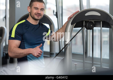 Personal Trainer Showing Ok Sign To Client - Group Of People Exercising On Elliptical Walker In Gym Or Fitness Club Stock Photo
