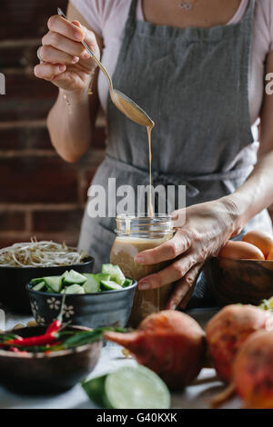 A woman is pouring warm peanut sauce into a jar. Stock Photo