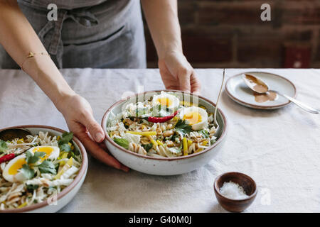 A woman is placing a bowl of Crunchy Veggie Bowl with Warm Peanut Dressing on the table photographed from the front view. Stock Photo