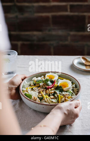 A woman is photographed while she is placing a veggie bowl on the table. Stock Photo