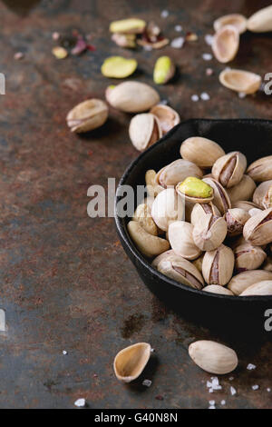 Salted roasted pistachios nuts with shell and salt  in  in black small cast-iron pan over old rusty iron textured background. Wi Stock Photo