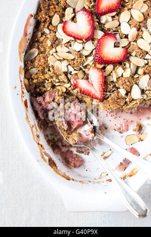 A portion of a large oval bowl of half eaten Strawberry and Rhubarb Breakfast Oat Crisp is photographed from the top. Stock Photo