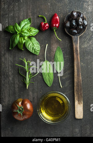 Vegetables and herbs on dark rustic wooden background. Greek black olives, fresh green sage, rosemary, basil herbs, oil, tomato, Stock Photo