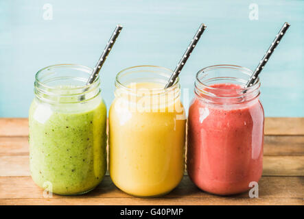 Freshly blended fruit smoothies of various colors and tastes in glass jars. Yellow, red, green. Turquoise blue background Stock Photo