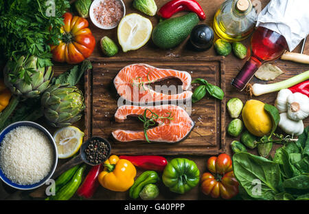 Raw uncooked salmon steak with vegetables, rice, herbs, spices and wine bottle on chopping board over rustic wooden background, Stock Photo