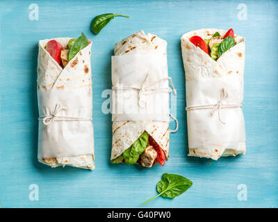 Healthy lunch snack. Tortilla wraps with grilled chicken fillet and fresh vegetables on blue painted wooden background. Top view Stock Photo