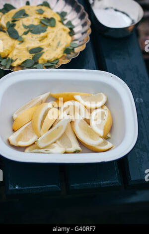 Fresh lemon slices in a white bowl and homemade mayonnaise with sage leaves, summer lunch scene Stock Photo