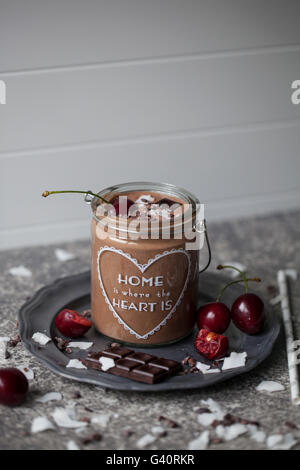 Chocolate coconut smoothie in a jar topped with cherry, dark chocolate, coconut flakes and cacao nibs Stock Photo