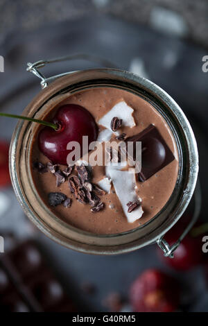 Chocolate coconut smoothie in a jar topped with cherry, dark chocolate, coconut flakes and cacao nibs Stock Photo