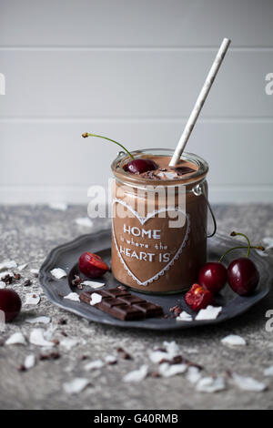 Chocolate coconut smoothie in a jar topped with cherry, dark chocolate, coconut flakes and cacao nibs Stock Photo