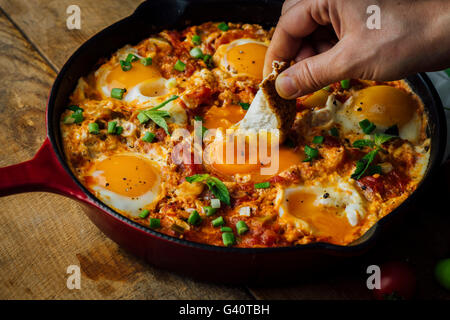 Dipping a traditional Turkish bread called simit into an egg dish made with eggs, tomatoes and green peppers called menemen or s Stock Photo