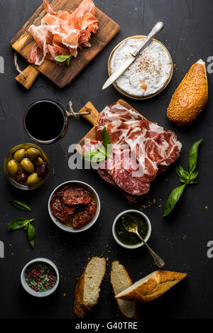 Wine snack set with empty wooden board in center. Glass of red, meat selection, mediterranean olives, sun-dried tomatoes, baguet Stock Photo