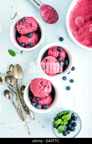 Homemade blueberry ice cream scoops with fresh berries and mint leaves in cups over light blue background, Top view, selective f Stock Photo