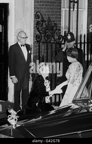 Prime Minister Margaret Thatcher curtseys to Queen Elizabeth II as she arrives for a dinner at 10 Downing Street, London, celebrating the 250th anniversary of the Prime Minister's office. Husband Denis Thatcher watches as a policeman salutes. Stock Photo