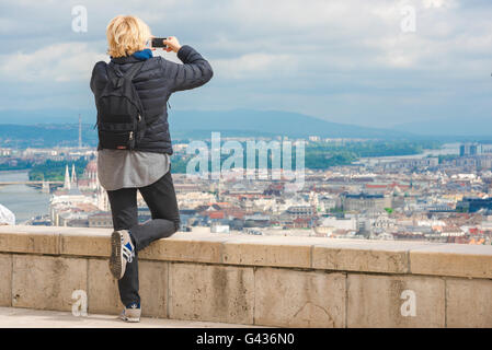 Woman solo traveler, a female tourist photographs the centre of Budapest from the top of Gellert-hegy Hill on the Buda side of the Danube, Hungary. Stock Photo