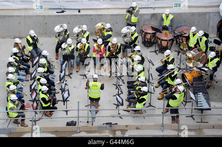 Over 40 brass and percussion musicians from the Guildhall School of Music and Drama perform a 'hard hat prom' on the floor of the schools new concert hall which is currently under development at Milton Court in London. Stock Photo