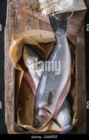 Two Raw uncooked seebass fish in wood box with dry herbs over old wooden background. Top view Stock Photo
