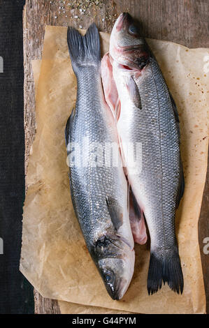 Two Raw uncooked seebass fish on baking paper with dry herbs over old wooden background. Top view Stock Photo