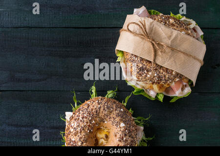 Two sprinkle seeds Whole Grain bagels with fried onion, scrambled eggs, green salad and prosciutto ham over dark wooden textured Stock Photo