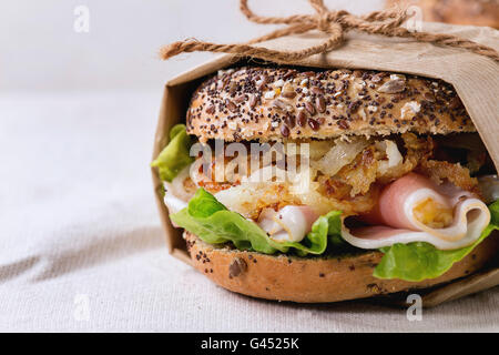 Papered Whole Grain bagel with fried onion, green salad and prosciutto ham over white linen tablecloth. Close up Stock Photo