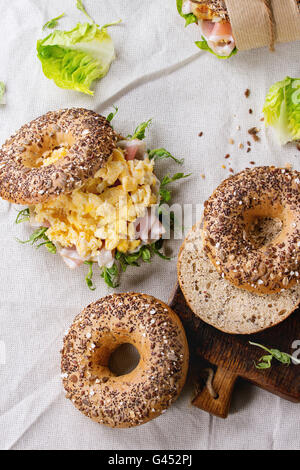 Empty and staff Whole Grain bagels with scrambled eggs, pea sprout, fried onions and prosciutto ham, making on white linen table Stock Photo