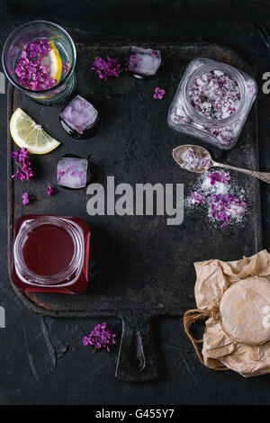 Lilac products collection. Glass jar of lilac flowers in sugar,glass of lilac water with lemon, ice cubes with flowers and jar o Stock Photo