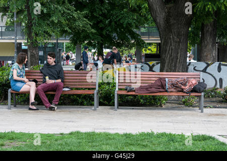 A homeless man sleeping on a park bench in Erzsébet Square (Erzsébet tér). The square  is the largest green area in Budapest in Stock Photo